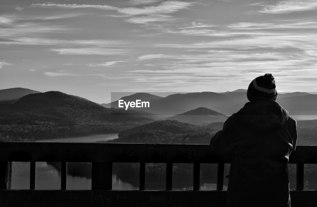 REAR VIEW OF MAN STANDING BY MOUNTAIN