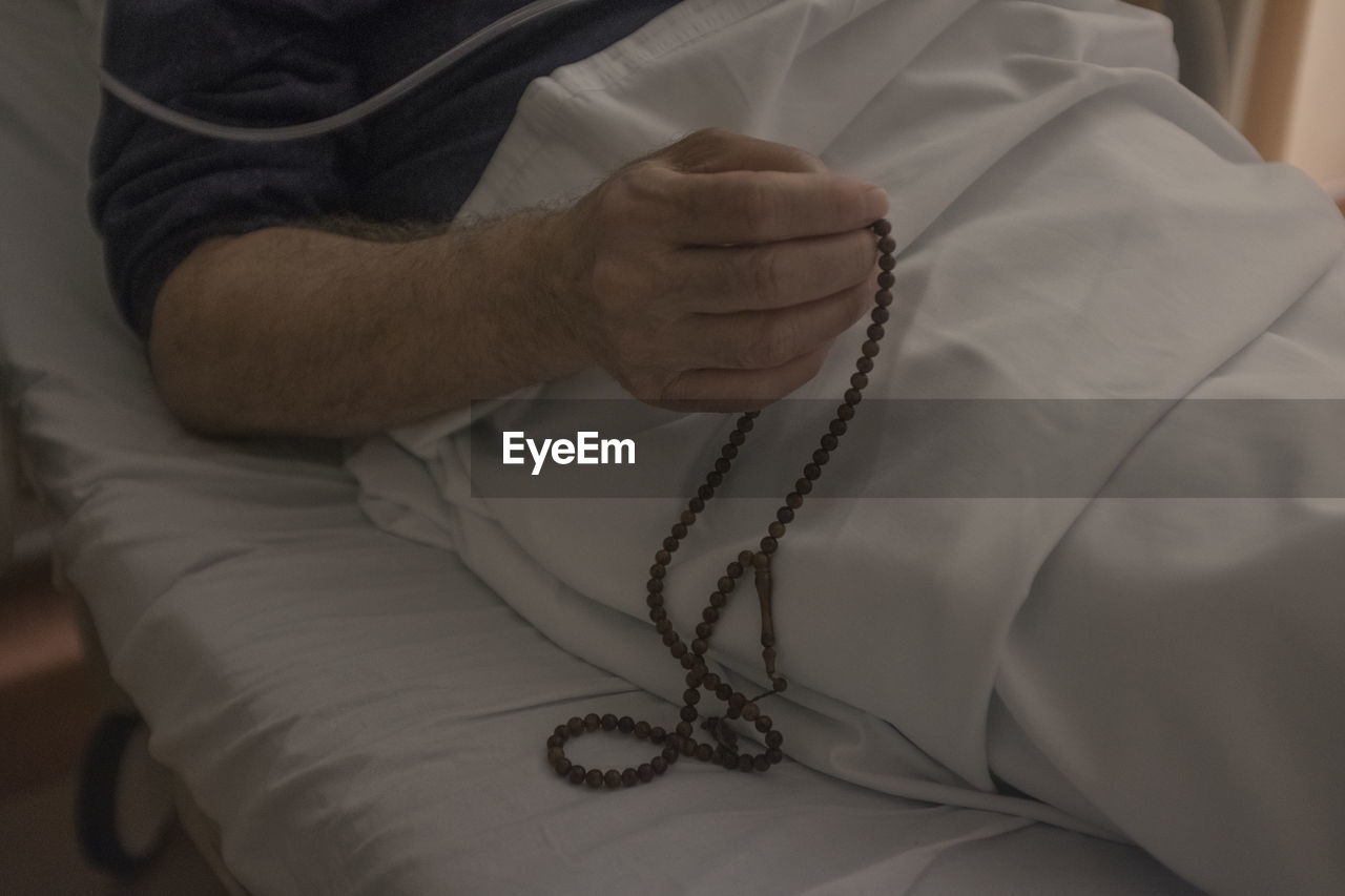 Midsection of patient praying with beaded necklace in hospital
