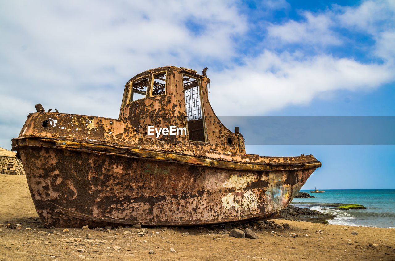 Old abandoned boat at beach against sky
