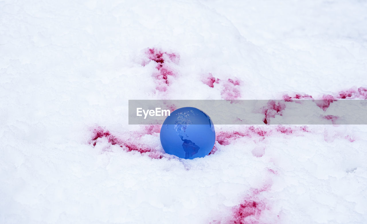 The concept of symbolism. crystal earth globe on snow with blood stains, selective focus