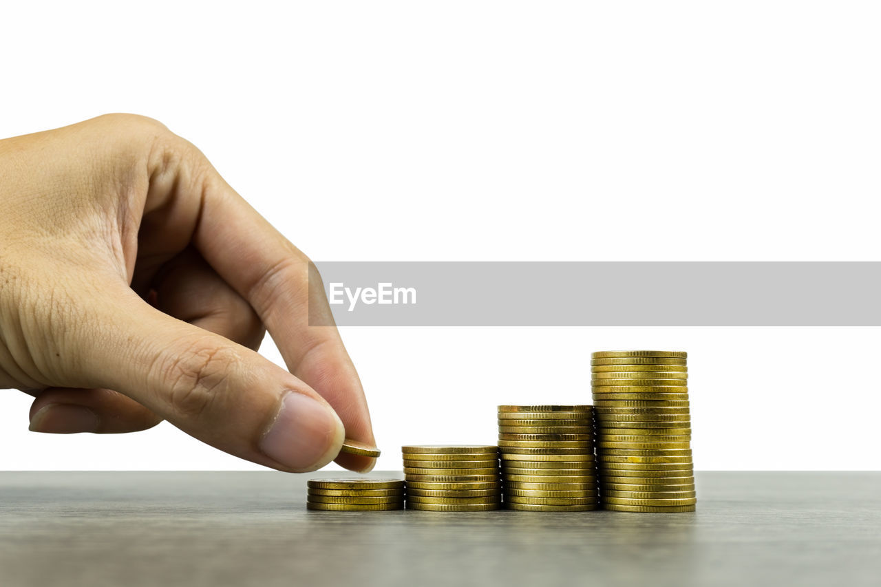 Cropped image of hand stacking coins on table against white background