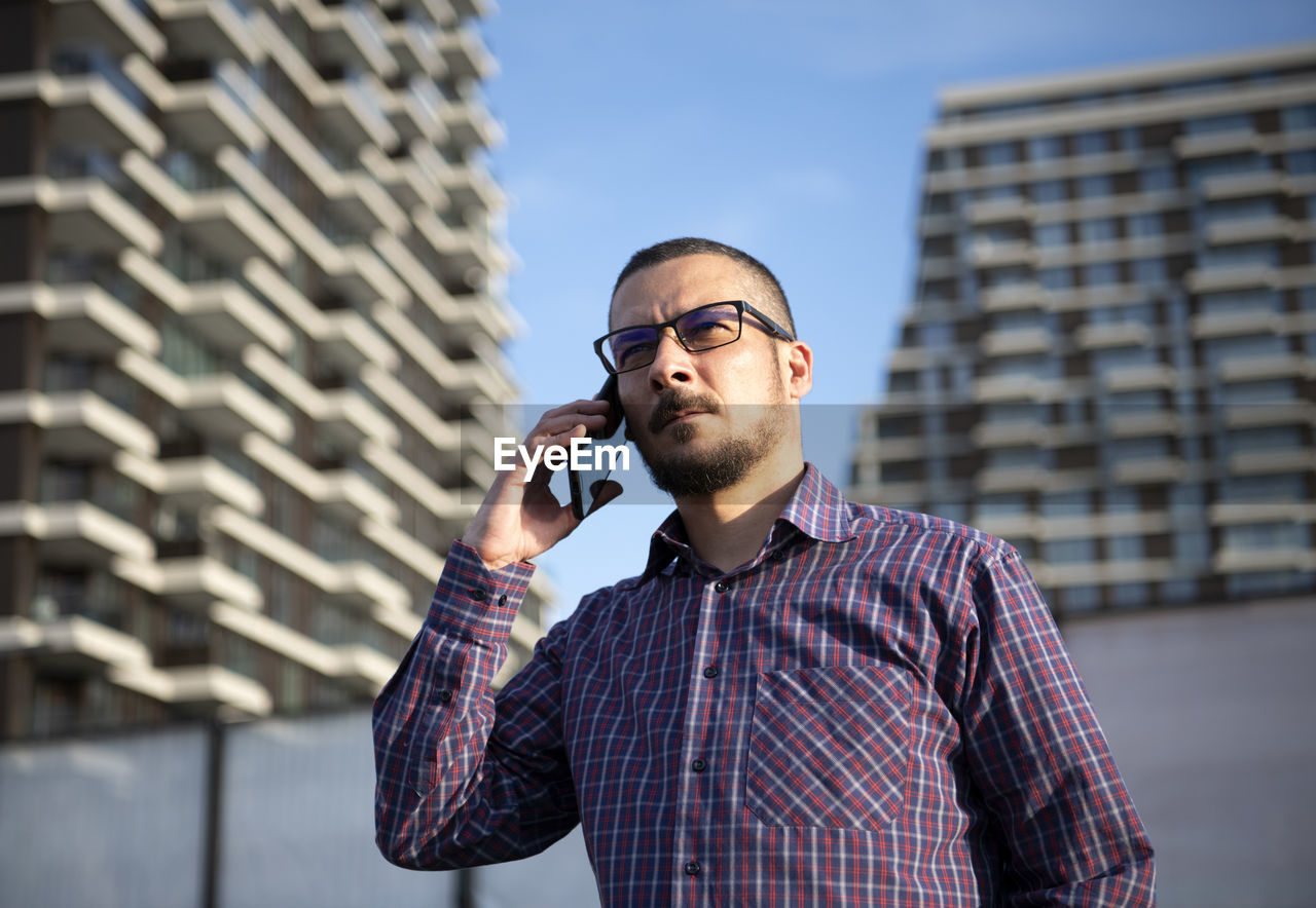 Low angle view of man talking over smart phone against buildings