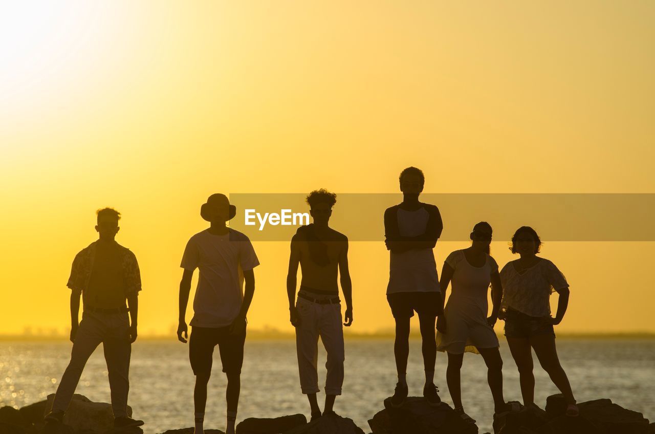 SILHOUETTE PEOPLE STANDING ON BEACH DURING SUNSET