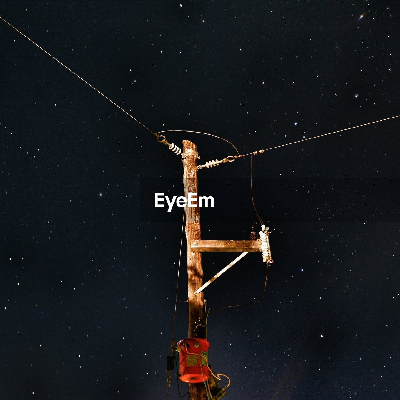 Low angle view of illuminated electricity pylon against star field in sky at night