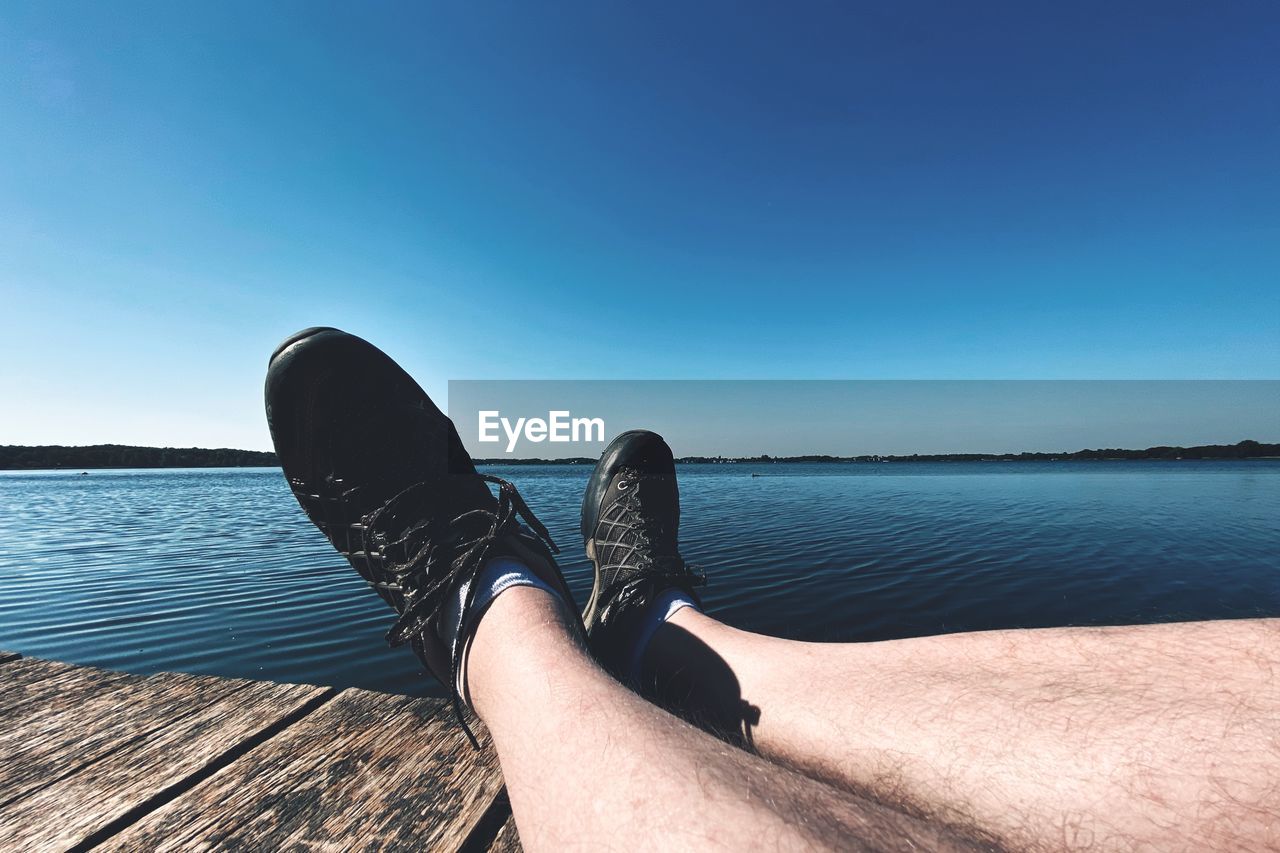 Low section of man sitting on pier by sea against sky