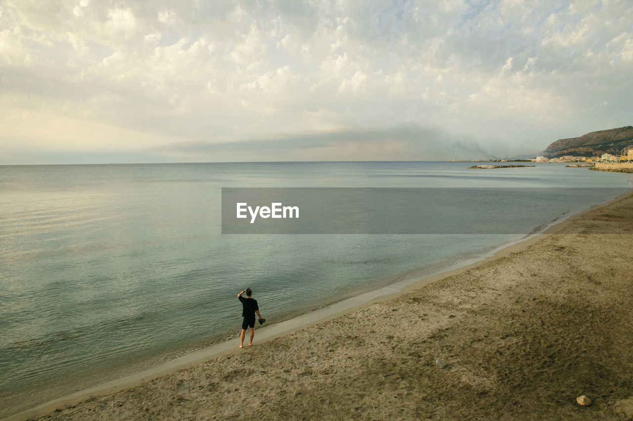 REAR VIEW OF PERSON STANDING ON BEACH