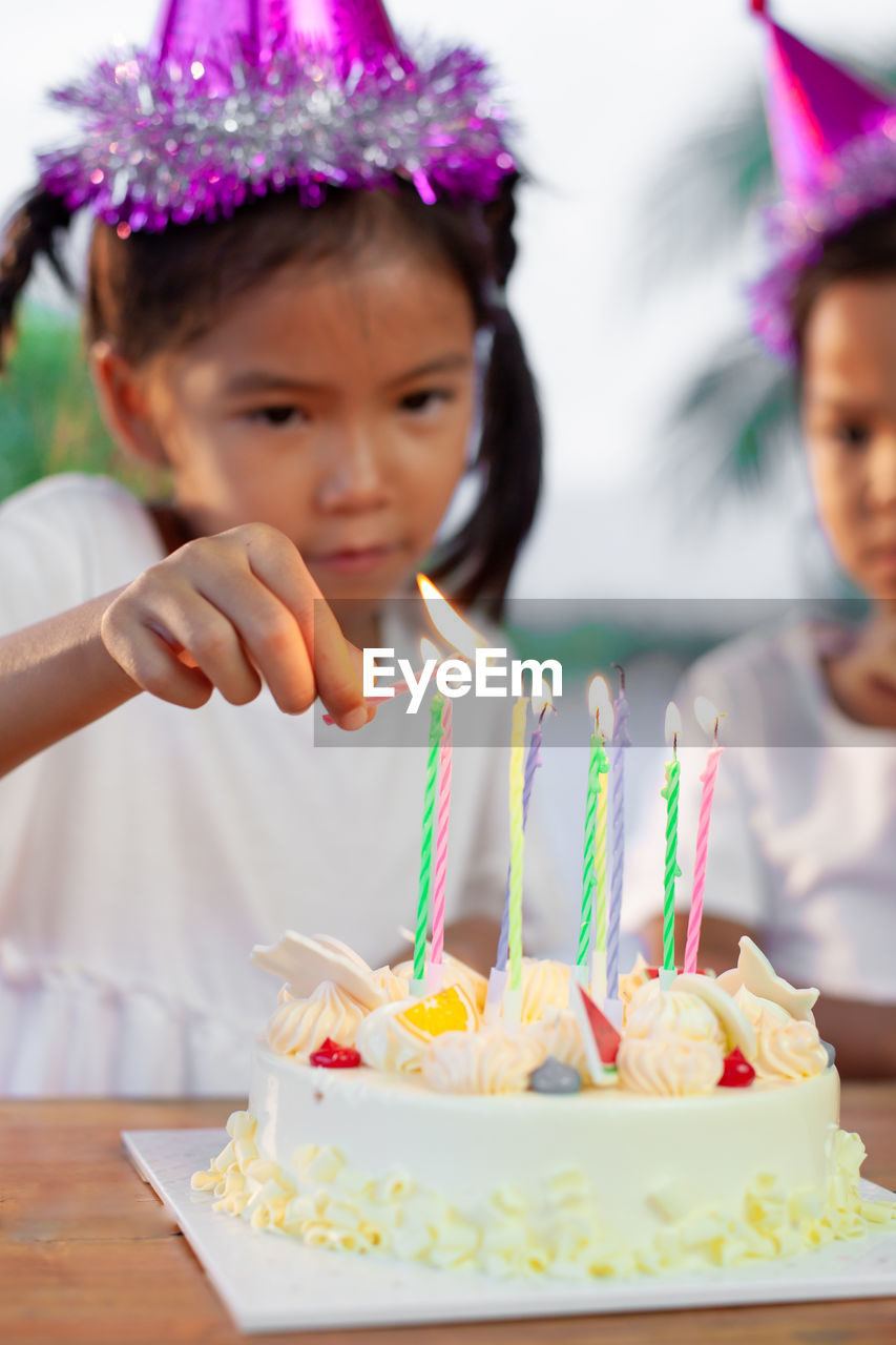 Girl burning candles on cake at table