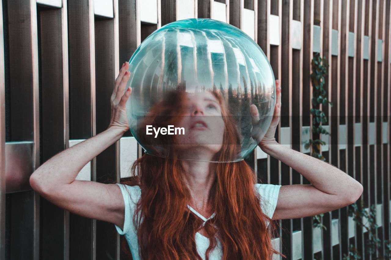 Close-up of young woman removing glass helmet from head against metallic railing