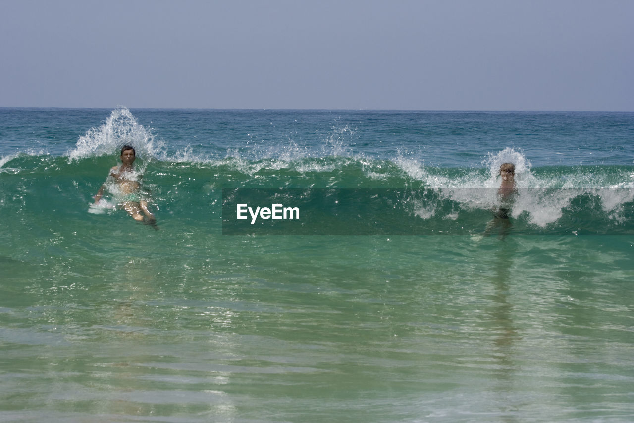 Father and son swimming in sea against sky