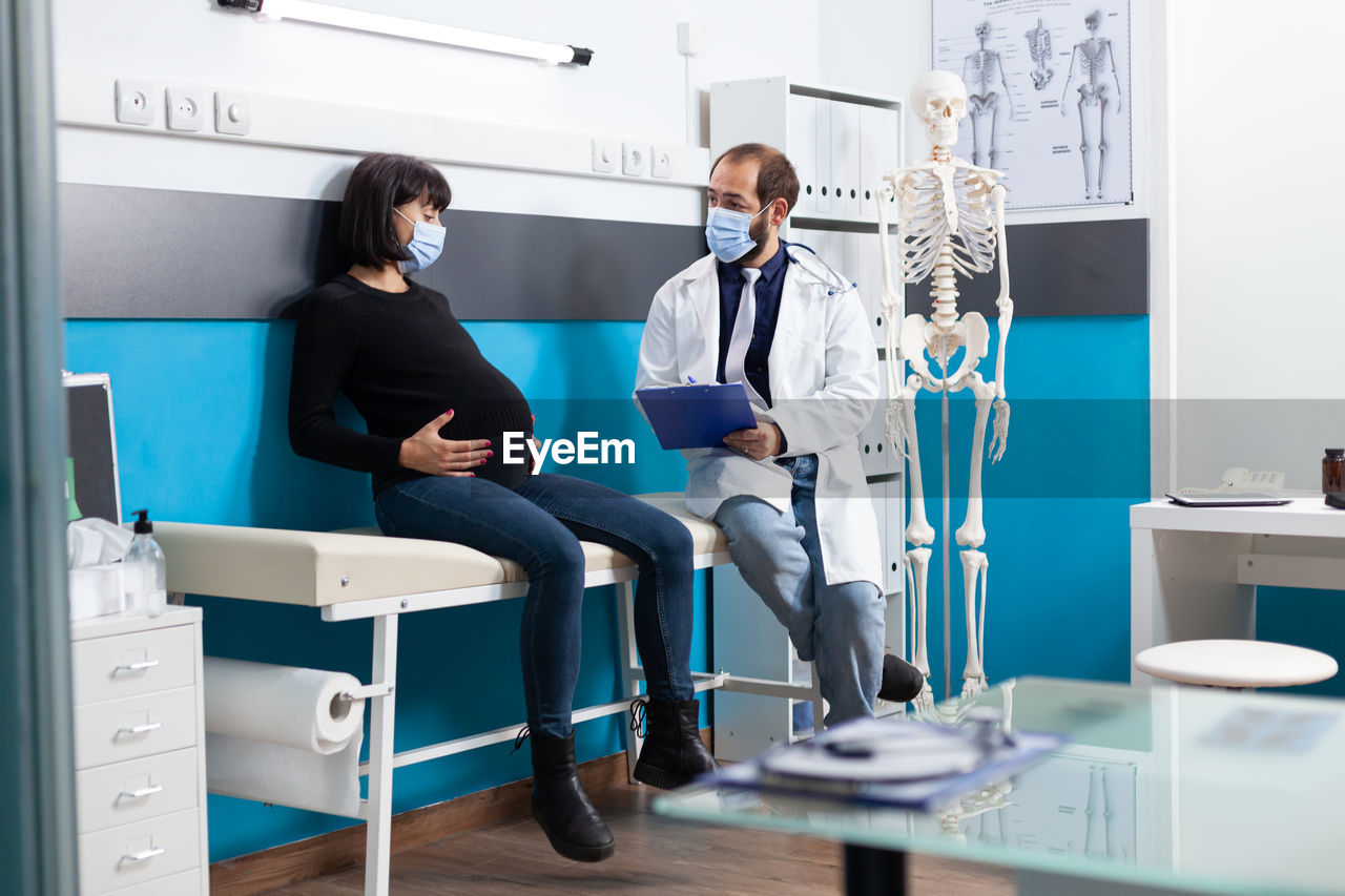 Doctor wearing mask examining pregnant woman in clinic