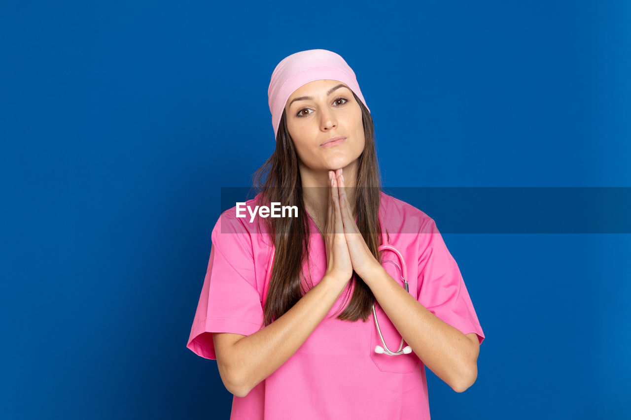 PORTRAIT OF BEAUTIFUL YOUNG WOMAN WEARING MASK AGAINST BLUE BACKGROUND