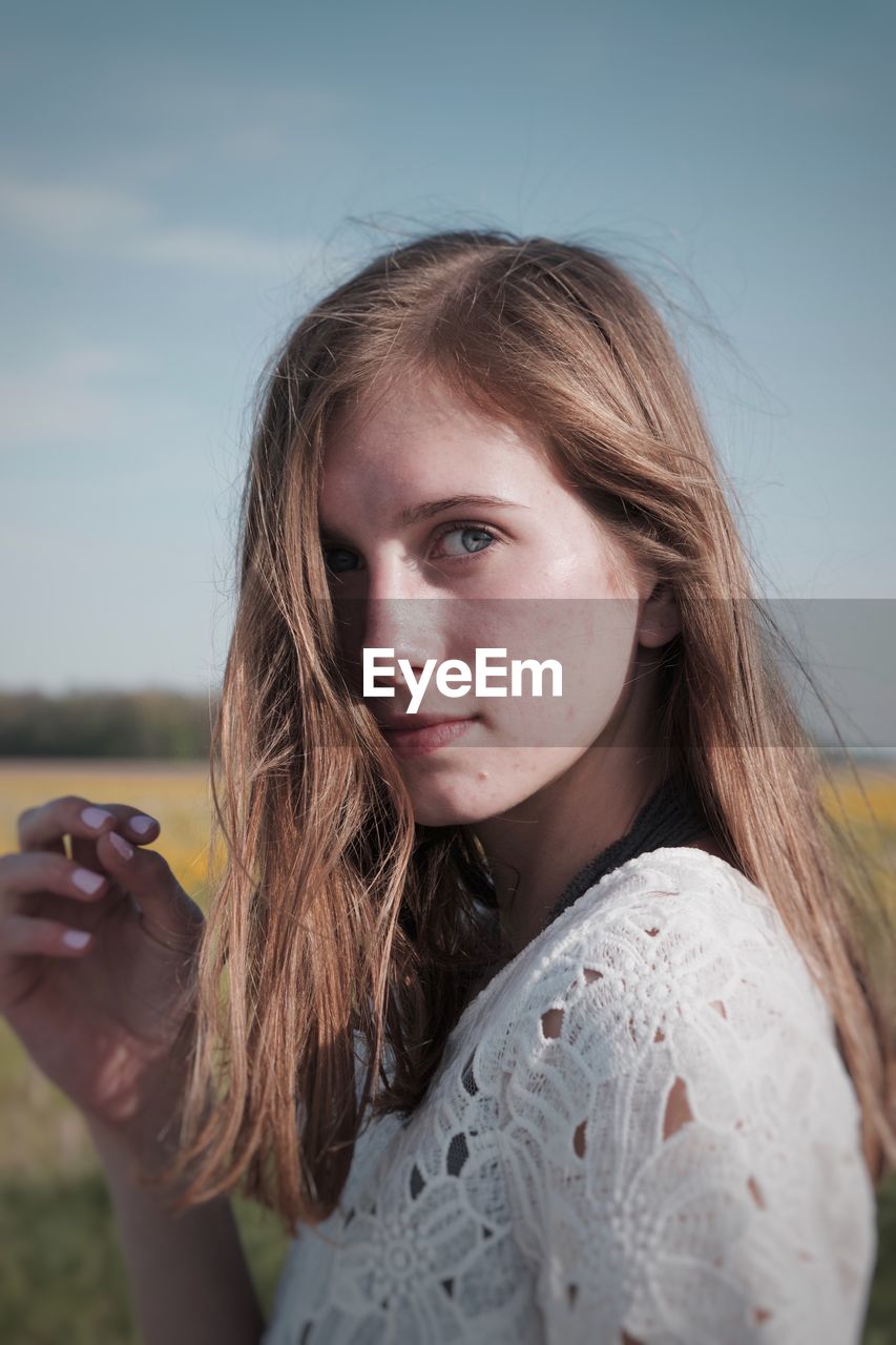 Close-up portrait of young woman against sky