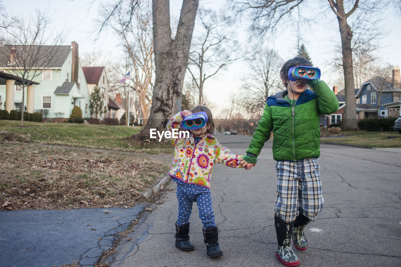 Siblings holding hands while looking through binoculars while playing on road