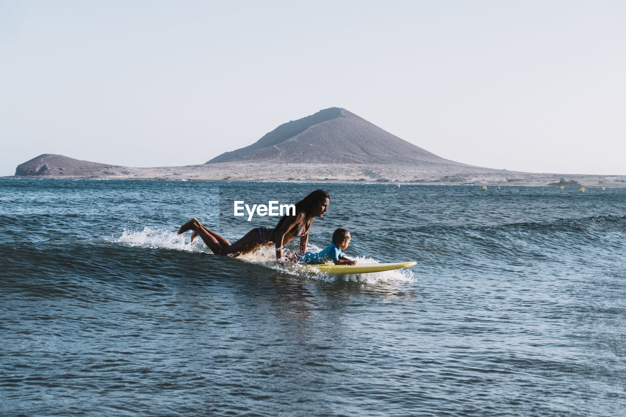 Pulled back view of mother and son surfing a small wave at sea