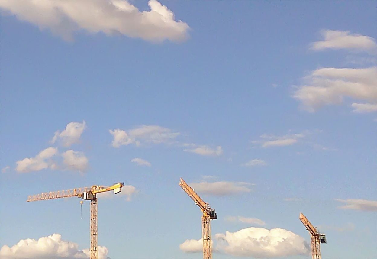 Construction cranes against cloudy sky