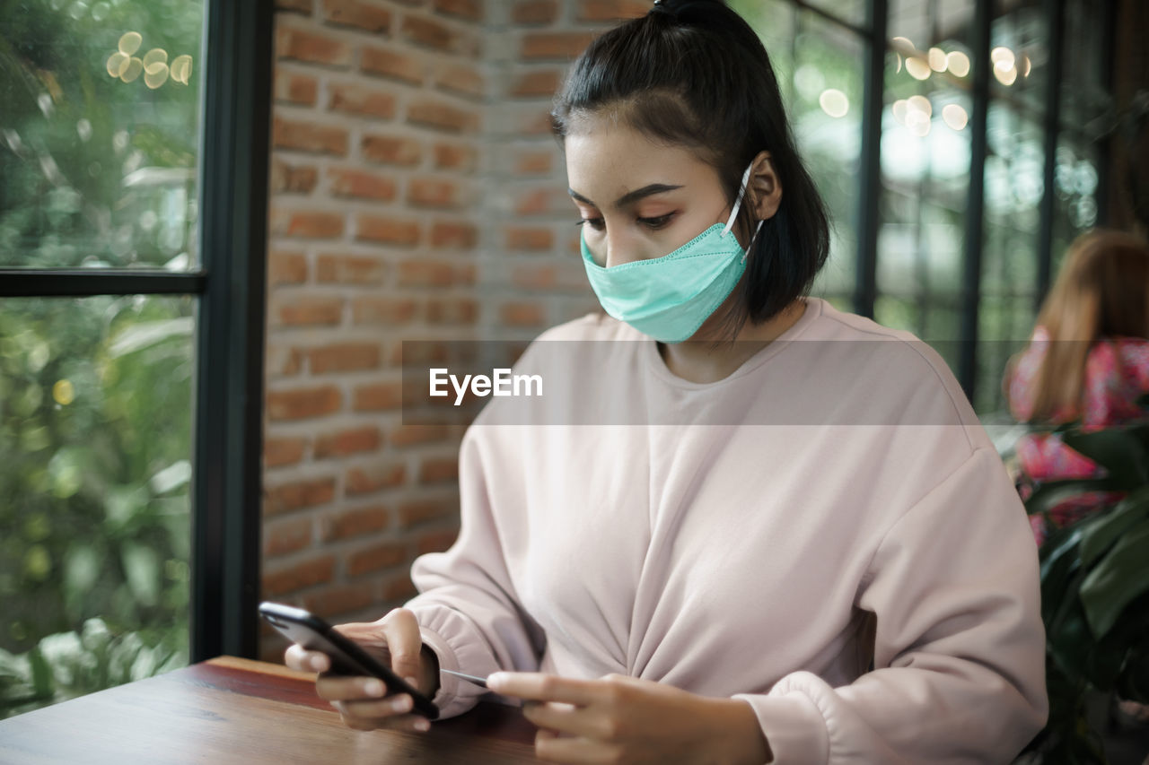 Young woman using smart phone on table at window