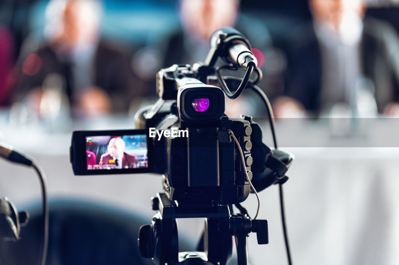 Professional digital camera recording presentation of a blurred speaker wearing suit