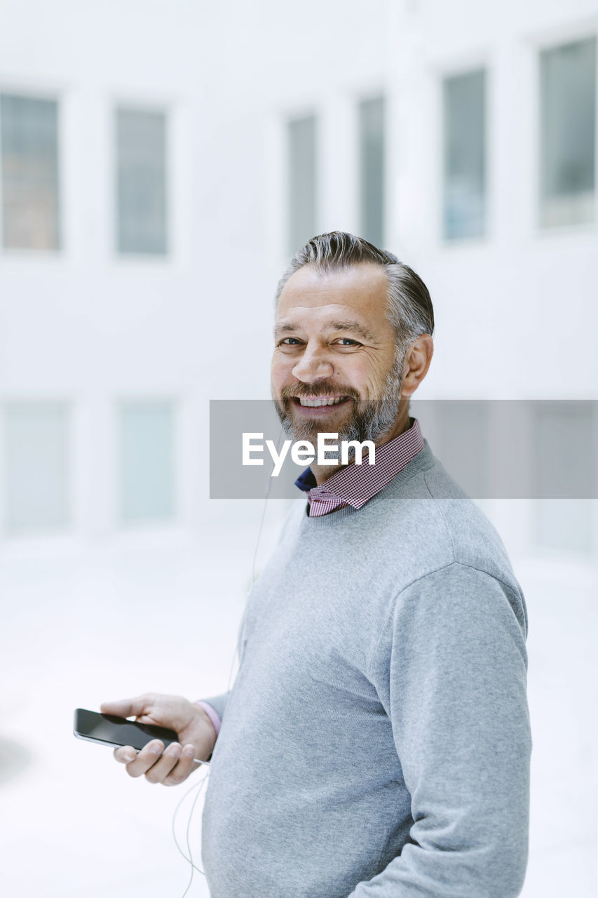 Portrait of happy businessman listening music through smart phone in office