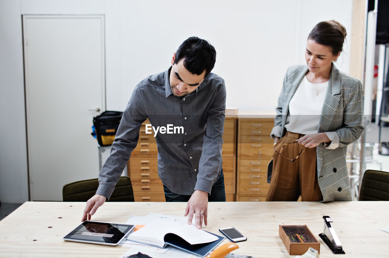 Businessman reading file and showing digital tablet to coworker at table in meeting