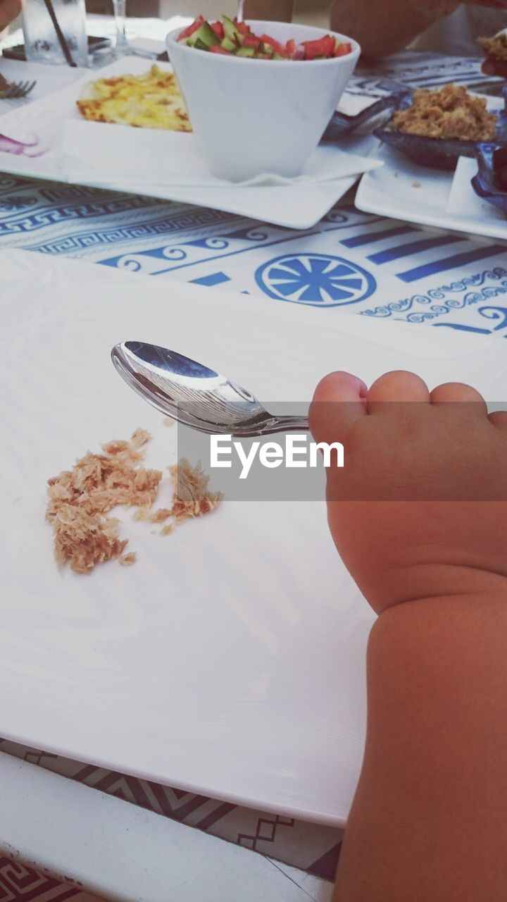 Cropped image on hand holding spoon against table