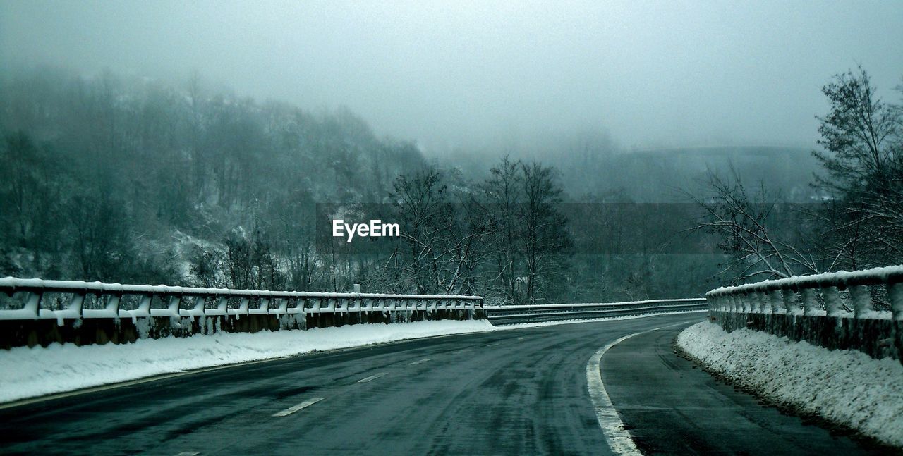 Road by snow covered trees against sky