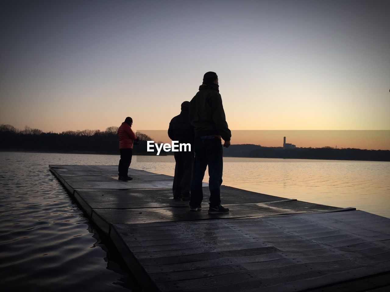 Men standing on floating platform at lake during sunset