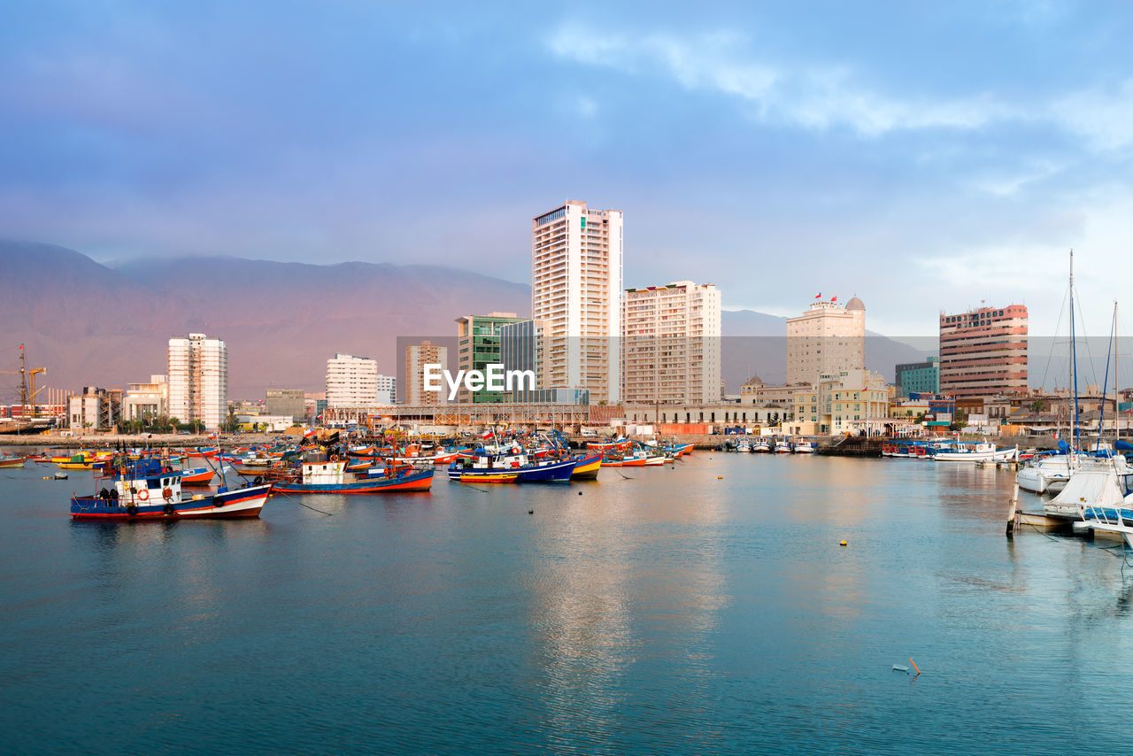 BOATS IN SEA BY BUILDINGS AGAINST SKY