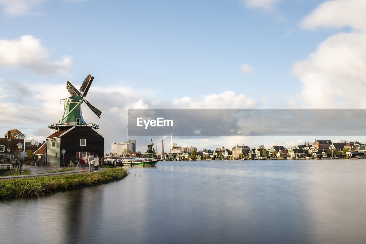 TRADITIONAL WINDMILL BY BUILDINGS AGAINST SKY WITH WATERFRONT