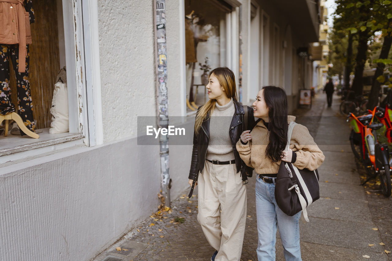 Female friends looking at store window while walking on sidewalk