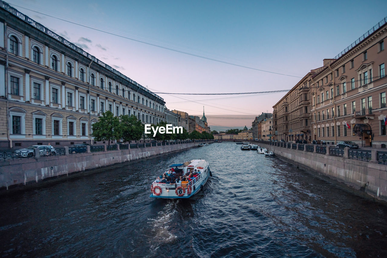 Cars on river amidst buildings in city against sky