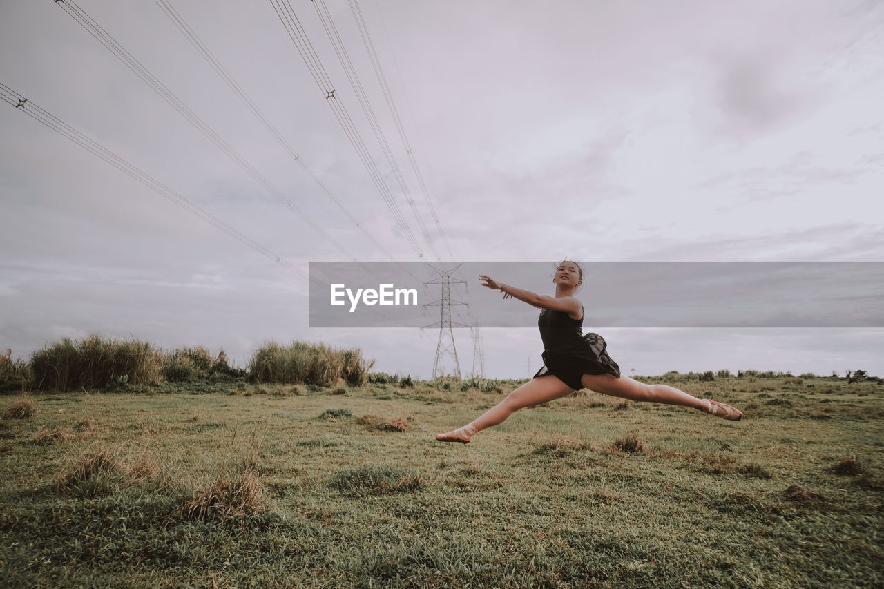 Ballerina jumping on grassy land against sky