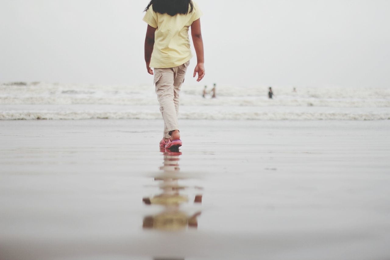 Low section of woman walking on beach against clear sky