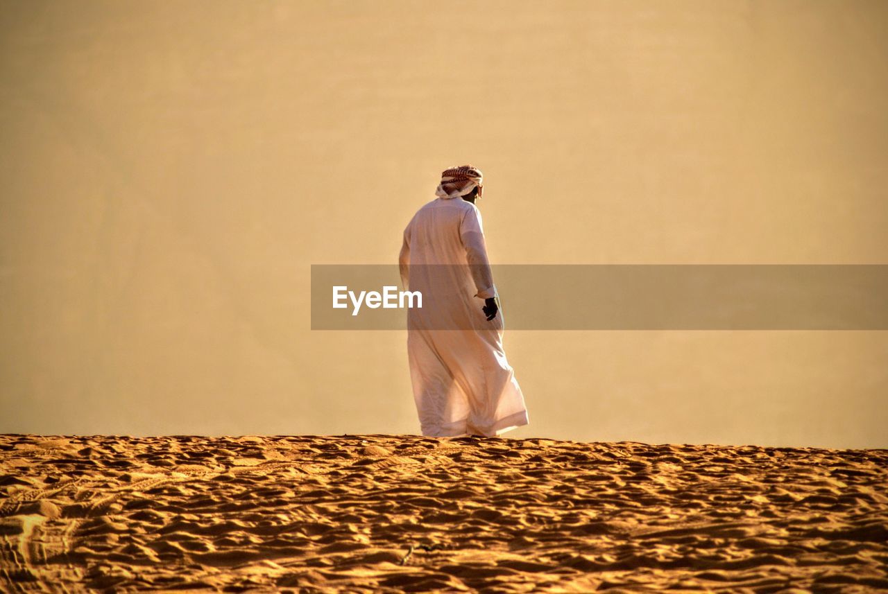 Rear view of man in traditional clothing walking on sand