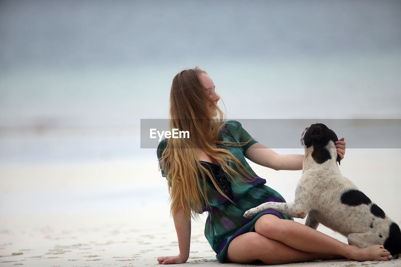 Full length of woman with dog sitting on beach