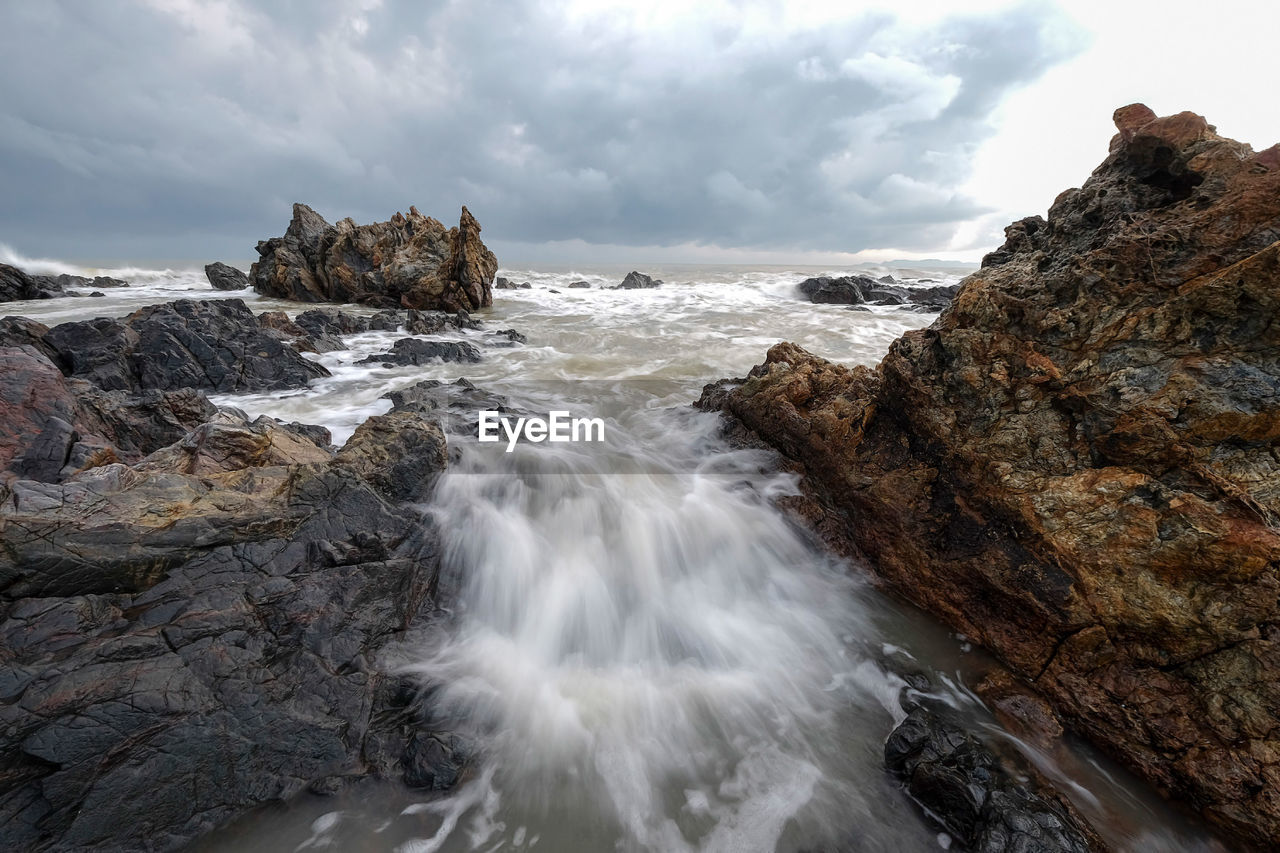 Long exposure image of waves crashing at beach against storm clouds