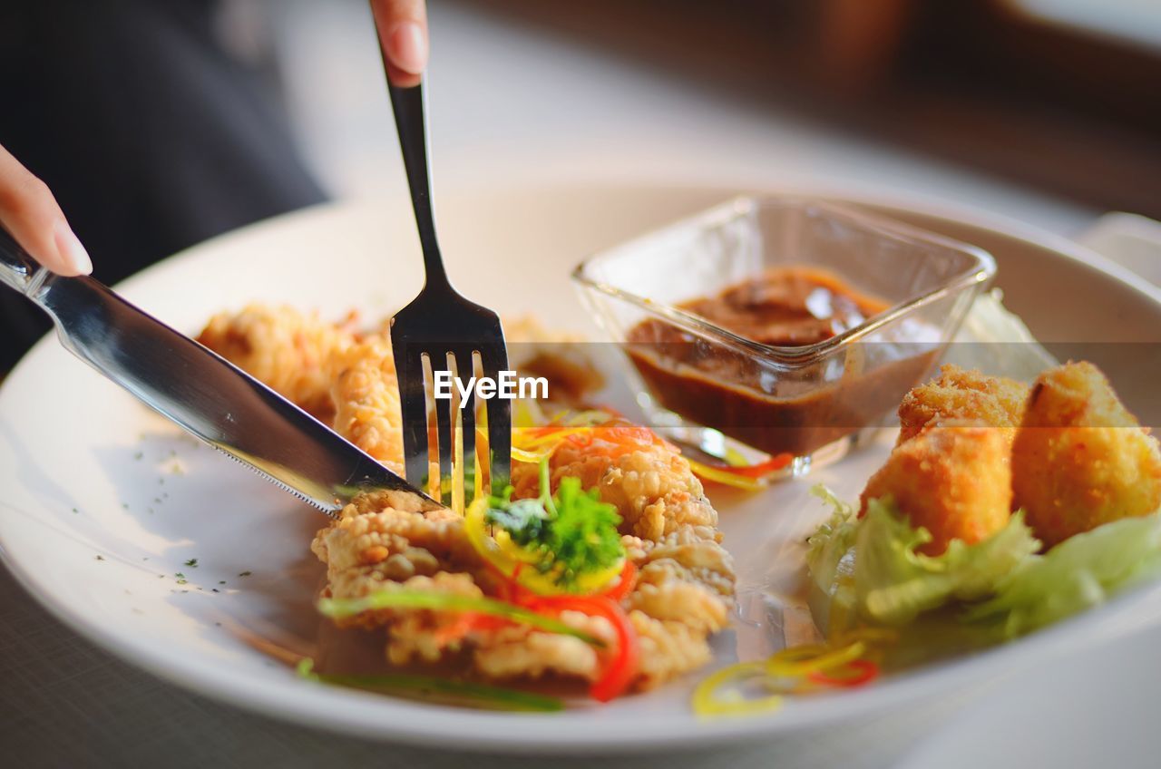 Cropped image of hands cutting fried chicken in plate