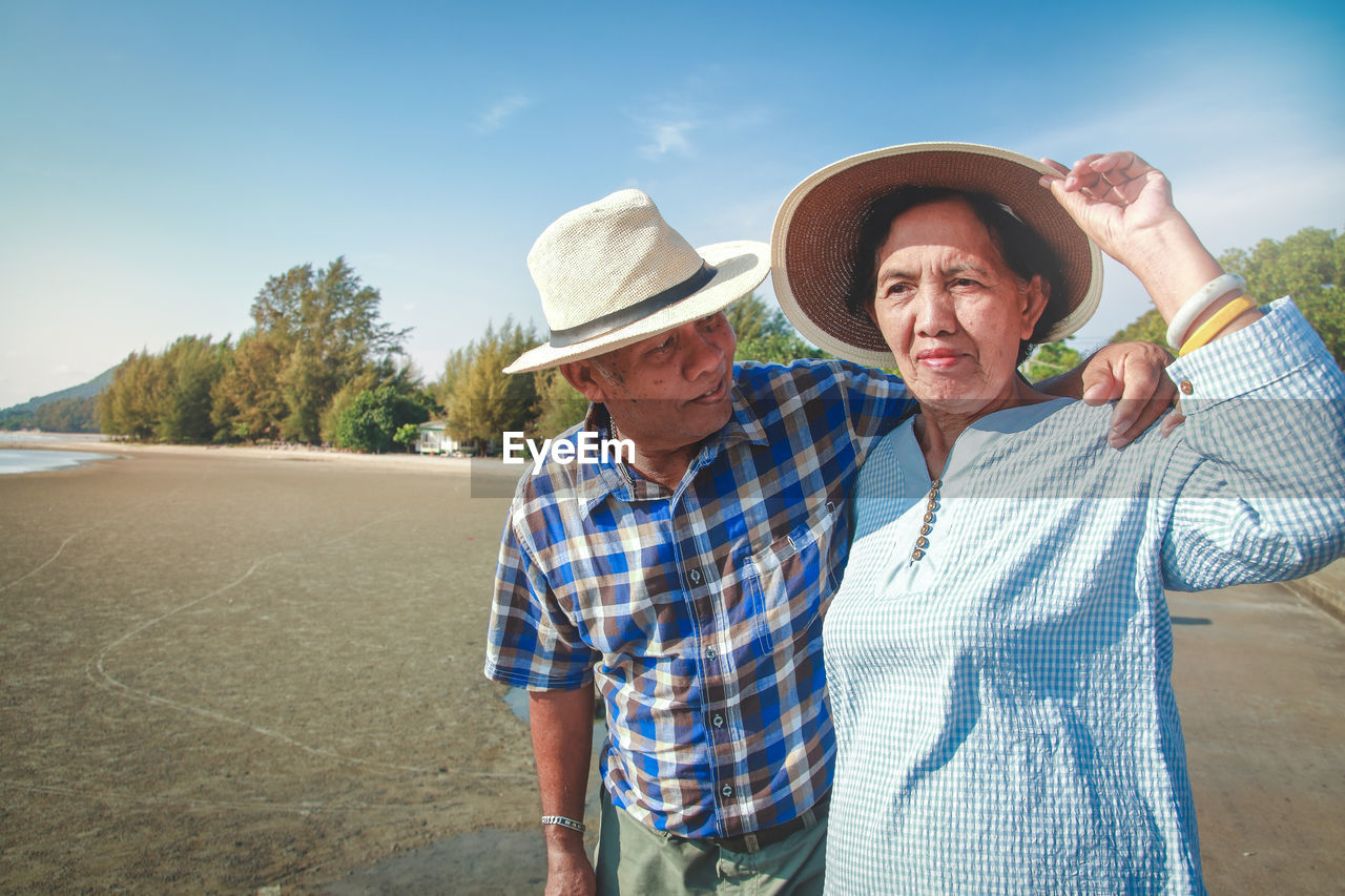 Senior couple standing at beach against sky