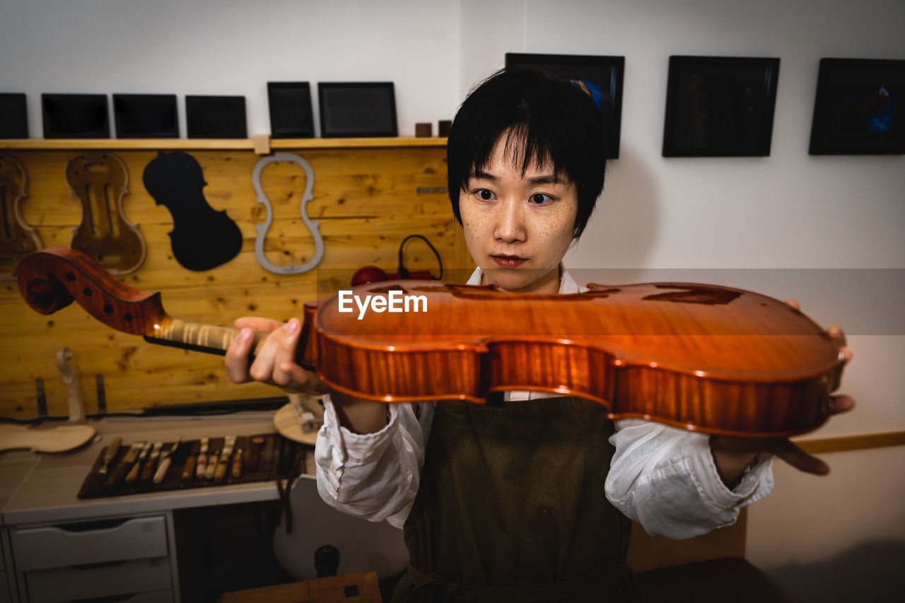 Young chinese woman violin maker checking the quality of her violin in the workshop