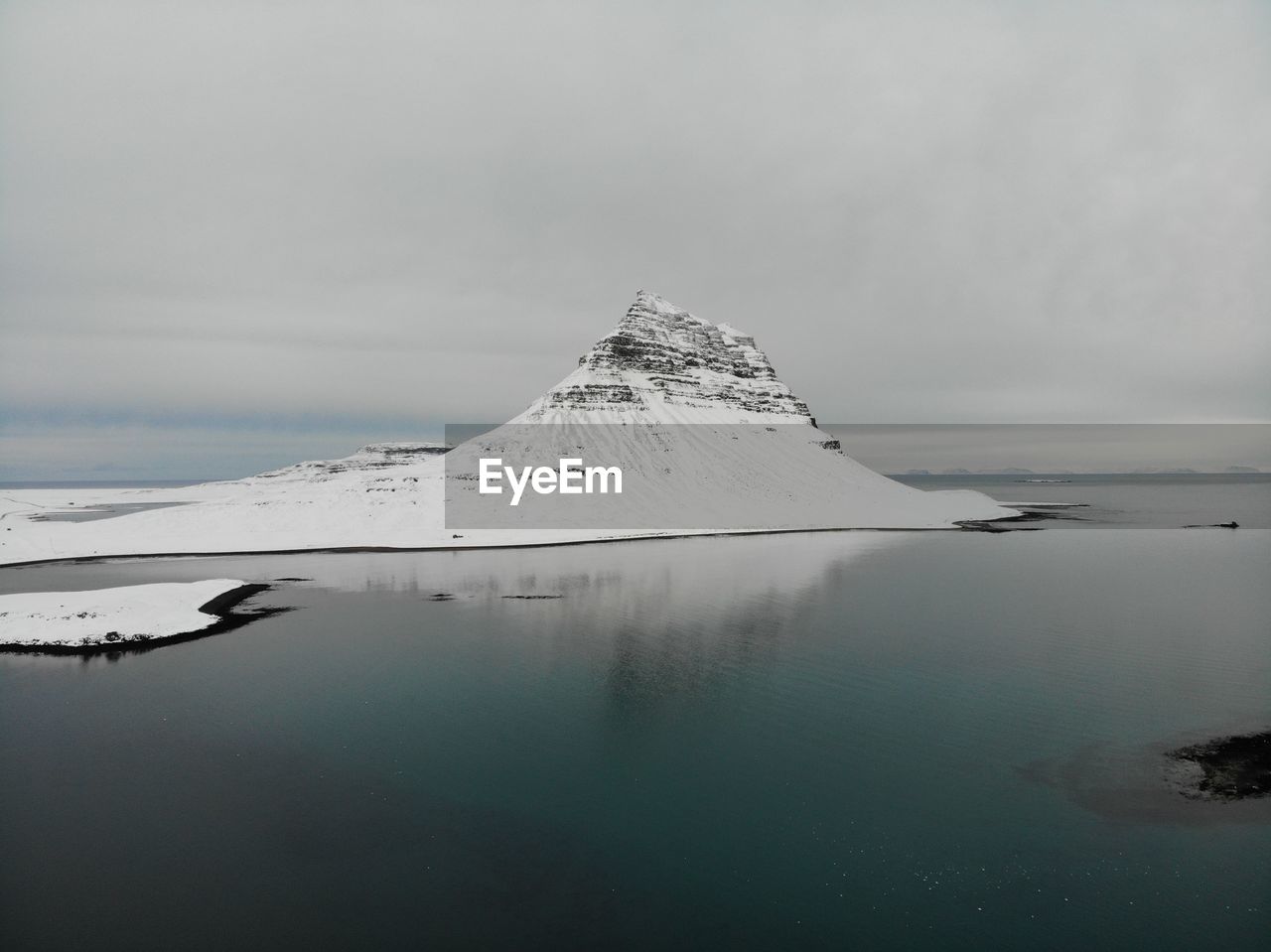 View of kirkjufjell mountain covered with snow over blue water in iceland