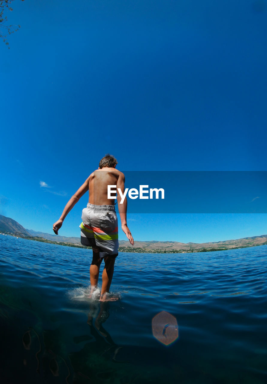Rear view of boy diving into lake chelan against blue sky