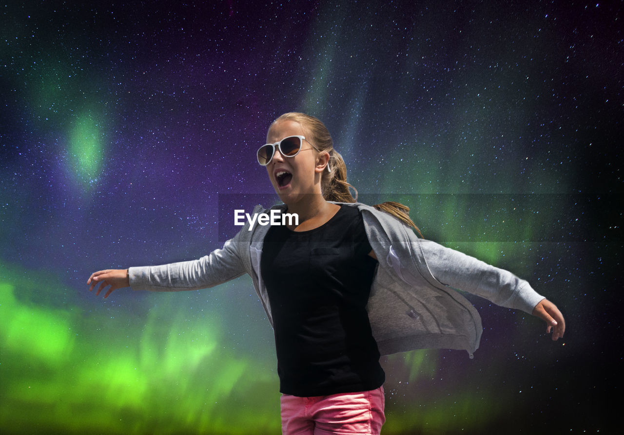 Low angle view of girl wearing sunglasses screaming while standing against northern lights