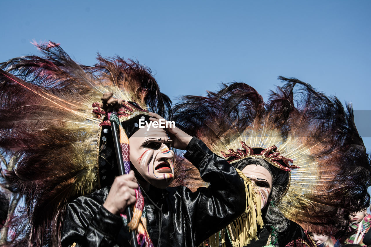 Low angle view of people wearing mask against sky on sunny day