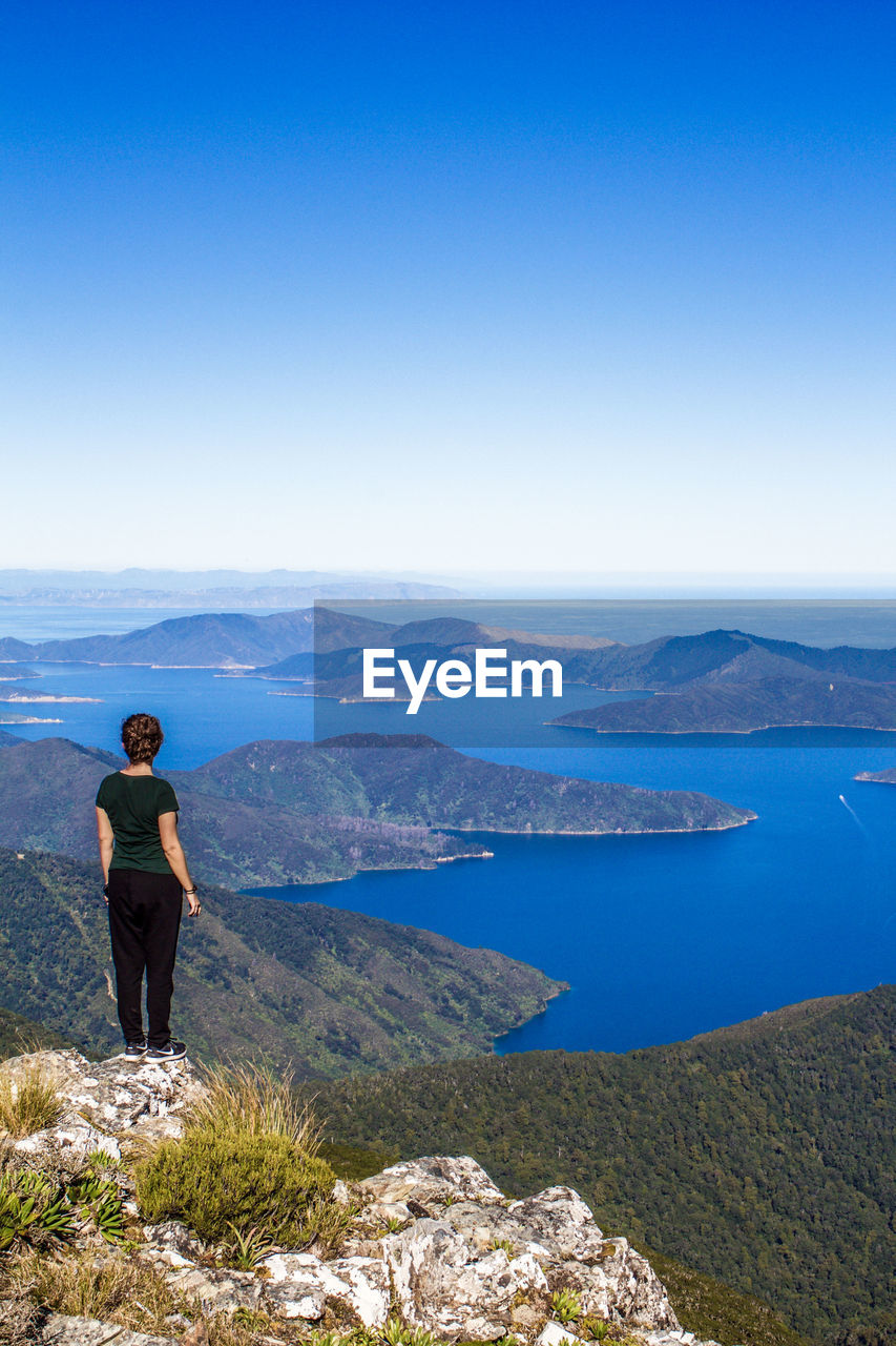 WOMAN STANDING ON MOUNTAIN AGAINST SKY