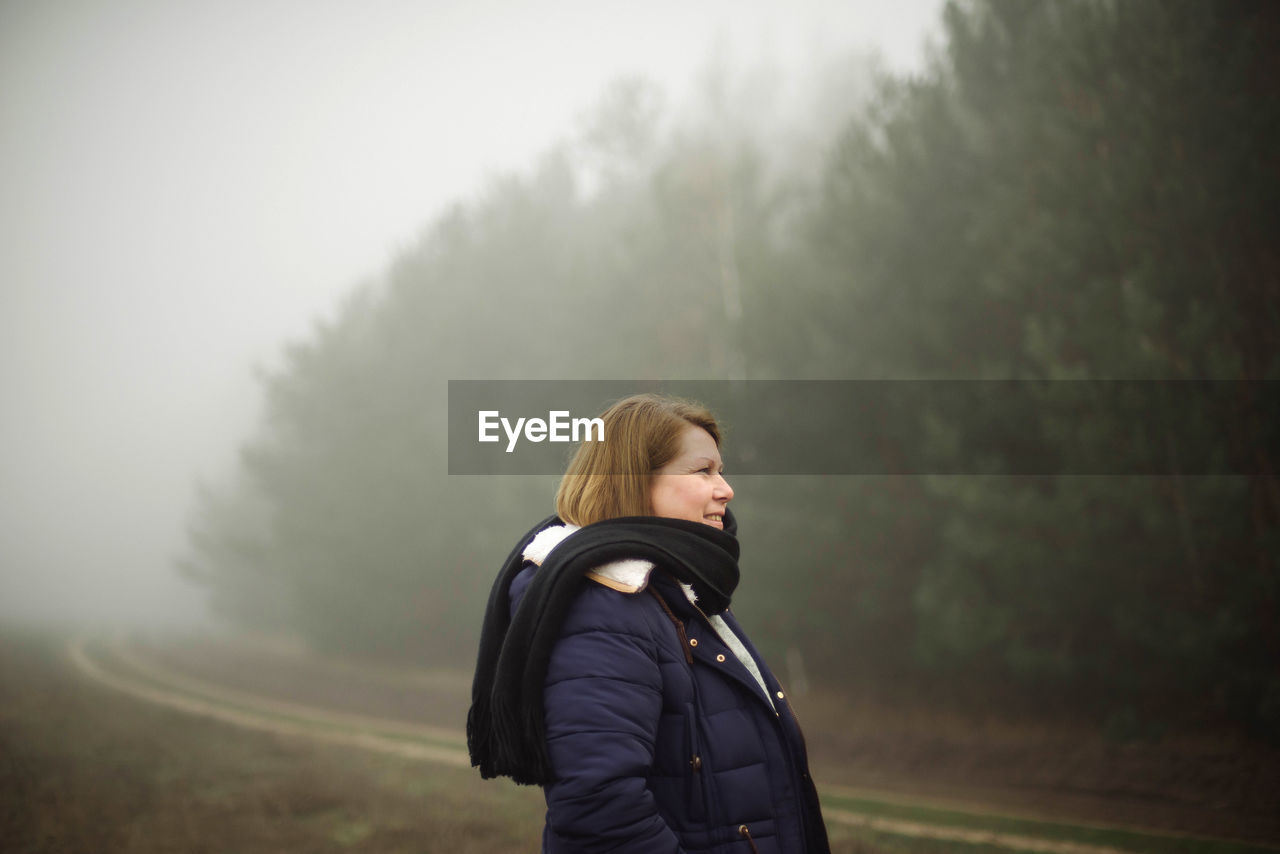 Woman standing by forest in foggy weather