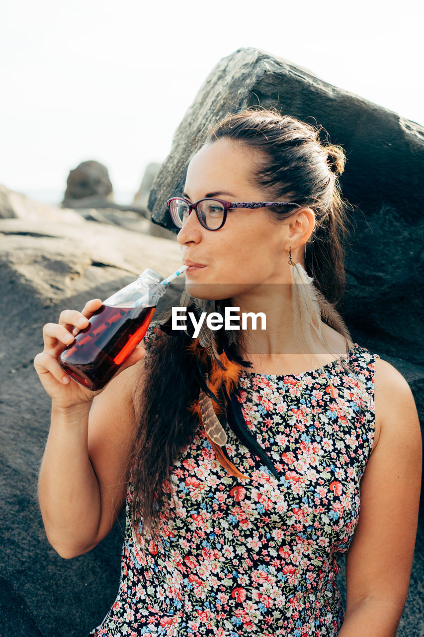 Woman looking away while drinking juice outdoors