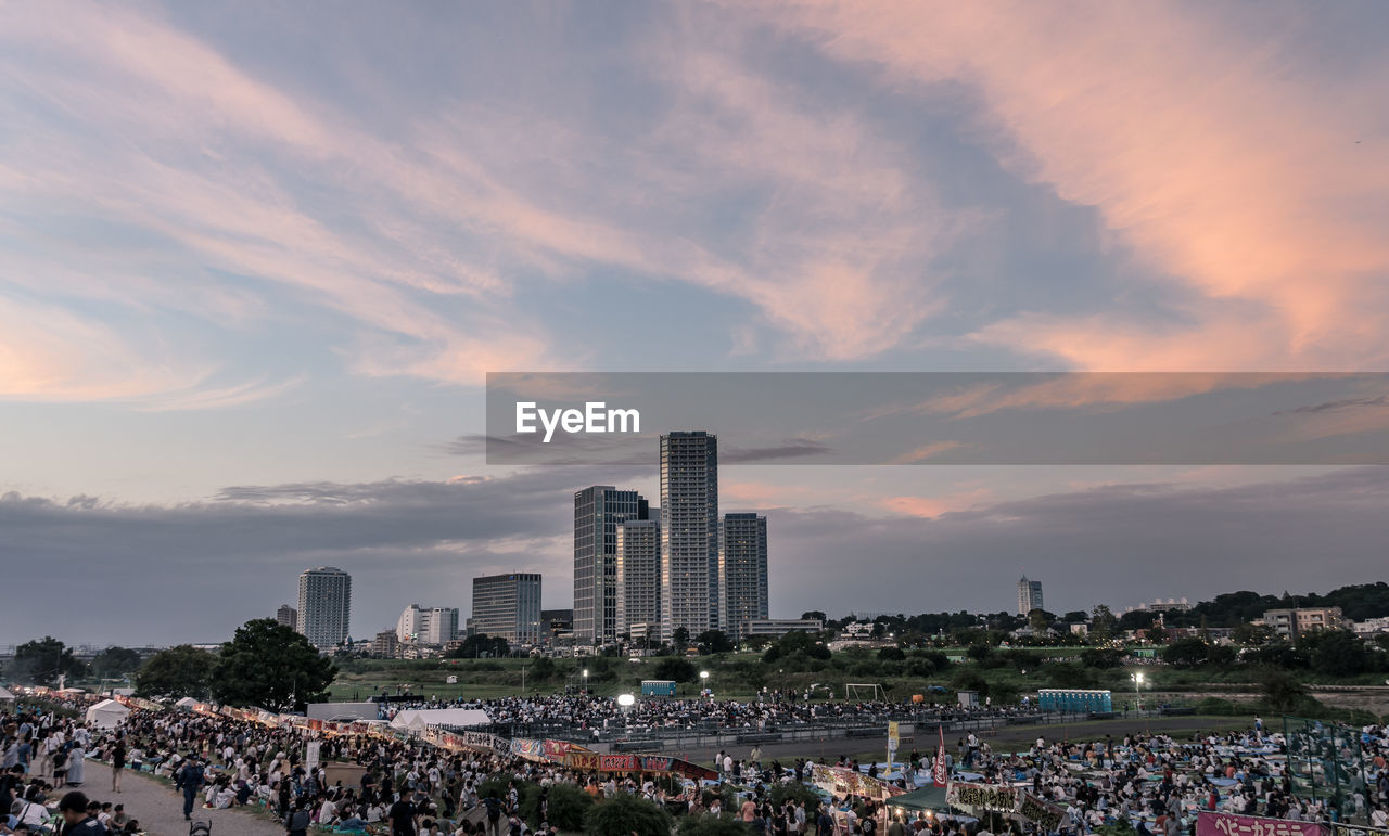 Group of people in city against sky during sunset