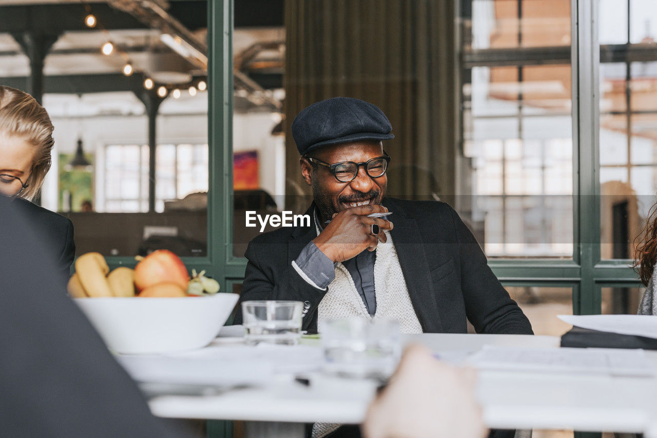 Happy businessman with hand on chin laughing during meeting at office