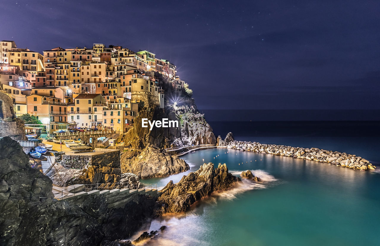 Panoramic shot of illuminated buildings by sea against sky