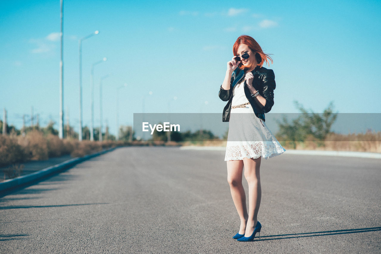 FULL LENGTH OF WOMAN STANDING ON ROAD AGAINST SKY