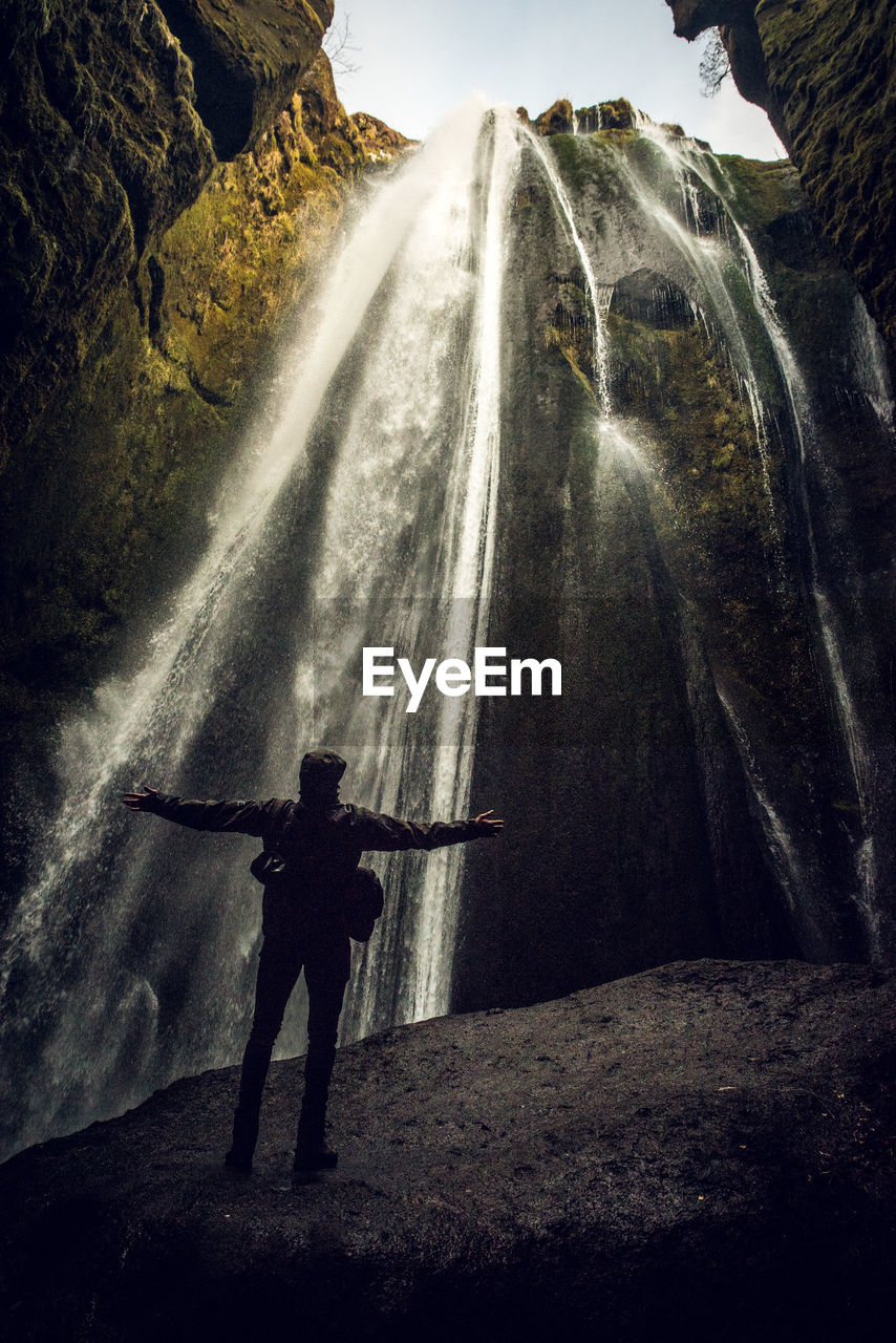 Rear view of man standing on rock against waterfall